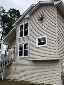 Two different sizes of vinyl windows installed on a house with tan siding