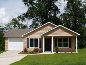 Beige vinyl siding on a home surrounded by lush green grass and towering trees