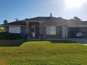 Aluminum storm panels fixed to the front of a dark brick home, on a sunny day