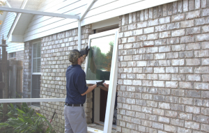 A man installing a new replacement window in a gray brick house