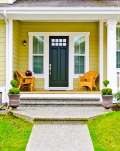 A front porch of a home with a green entry door and yellow siding