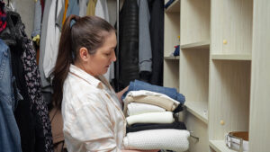 A brown-haired woman putting clothes away in a custom closet 
